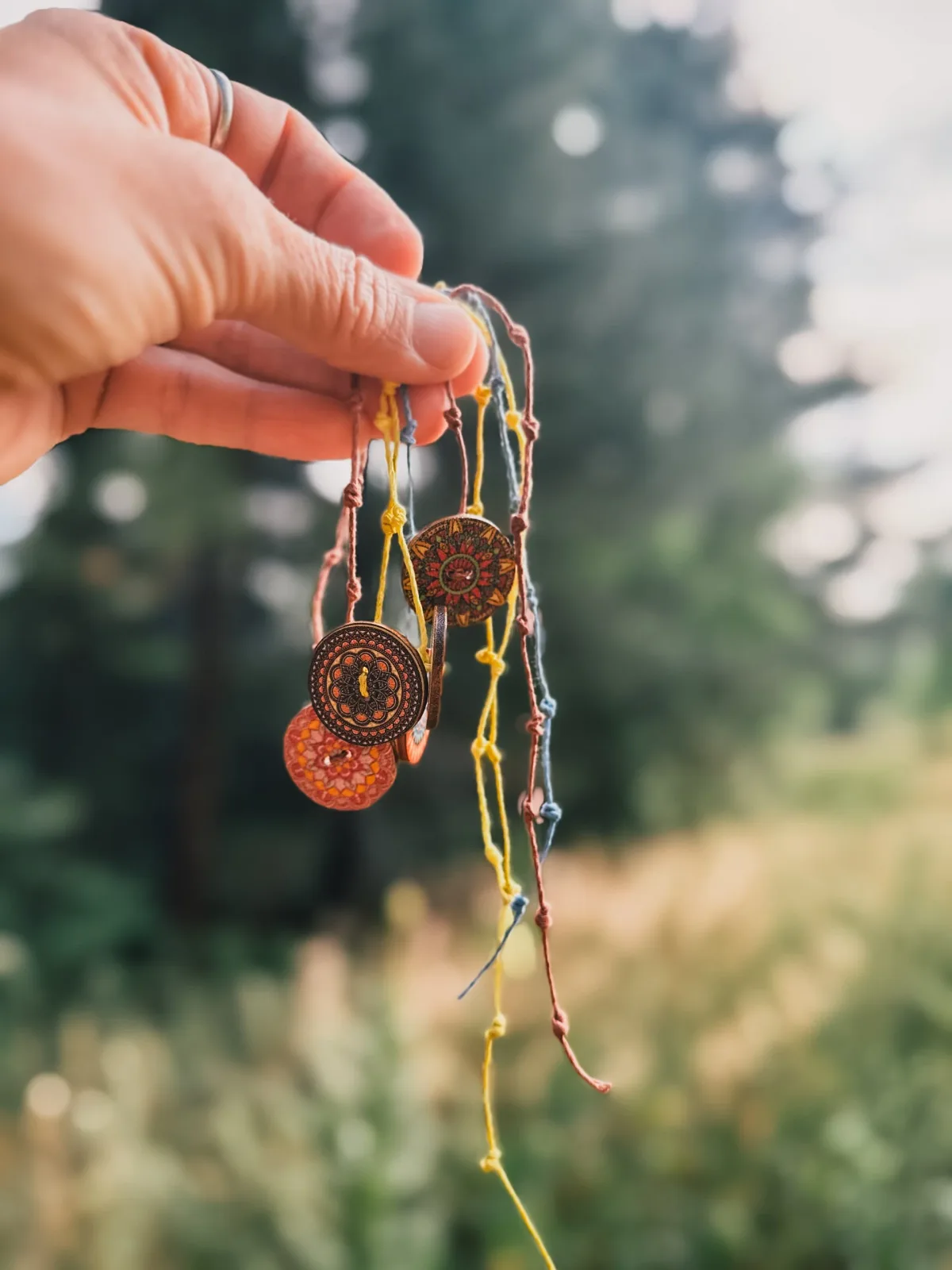 Handcrafted metal earrings with warm rust and bronze tones suspended from colorful strands.