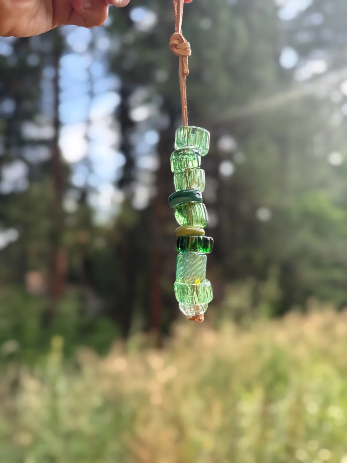 Handmade glass bead pendant with green and translucent segments suspended on twine.