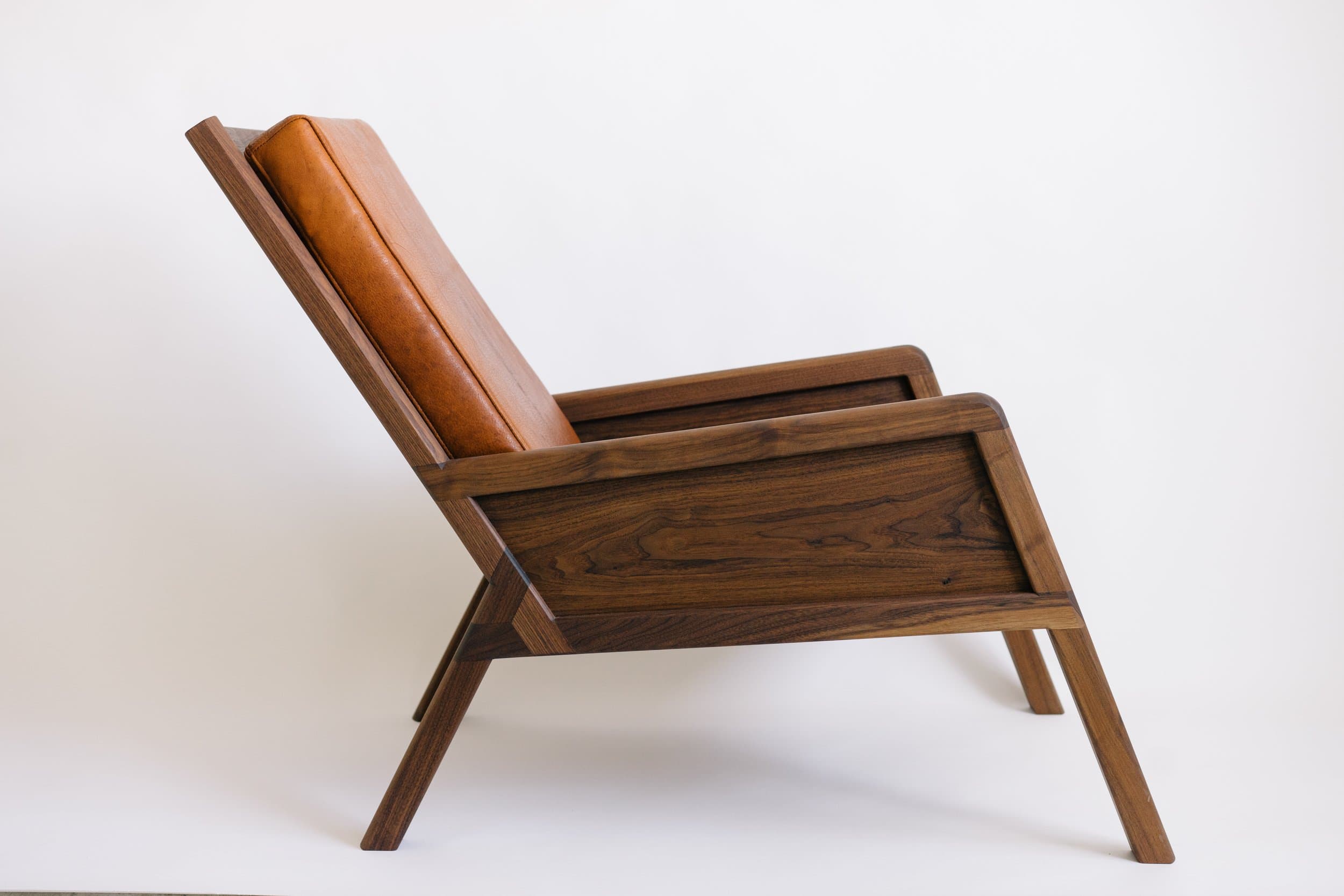 Mid-century modern wooden lounge chair with cognac leather cushioning.