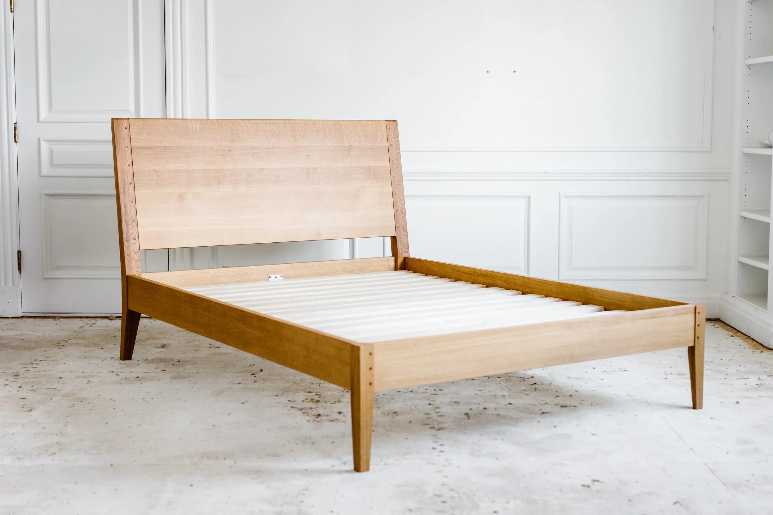 Wooden bed frame with light-wood construction and angled headboard in studio setting.